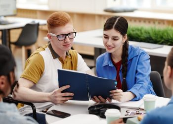 Vibrant shot of two smiling college students reading notes during group discussion in classroom